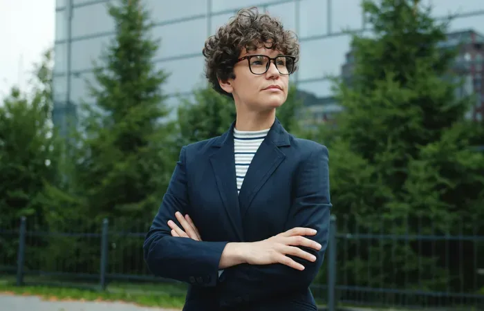Portrait of a confident small business owner in glasses and blazer, standing near modern offices and trees